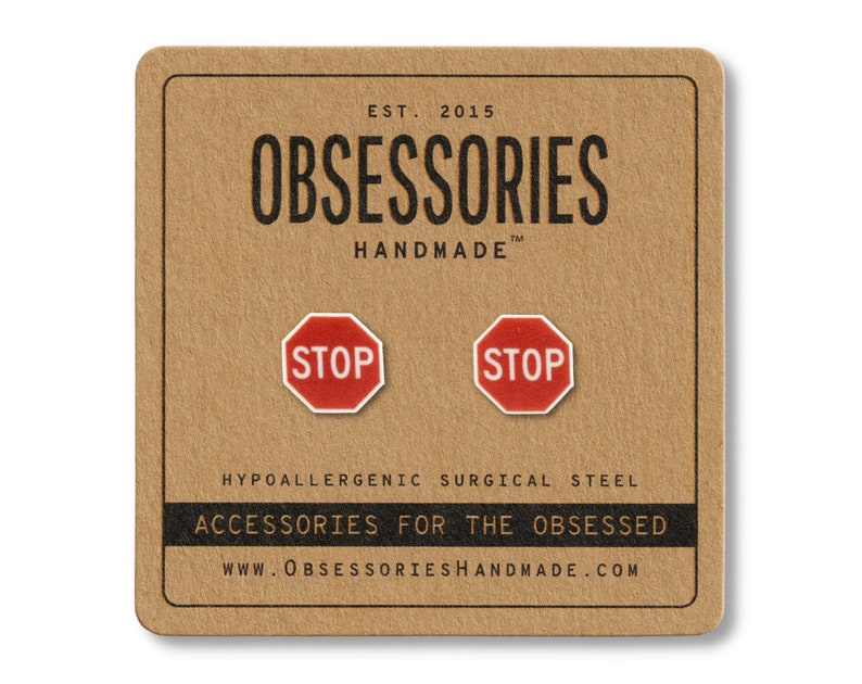 May include: A pair of red and white stop sign stud earrings on a brown card. The card has the text "OBSESSORIES HANDMADE" and "ACCESSORIES FOR THE OBSESSED". The earrings are made of hypoallergenic surgical steel.