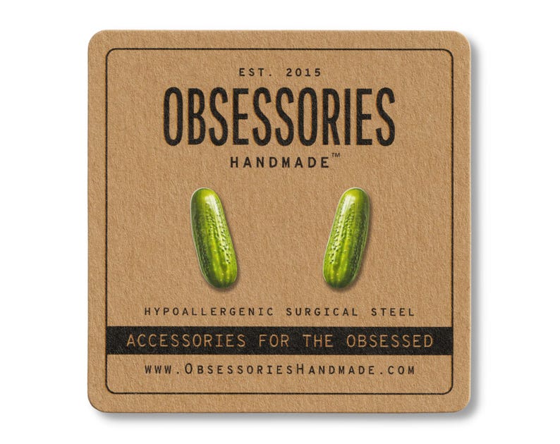 May include: A pair of green pickle earrings on a brown card. The card has the text "OBSESSORIES HANDMADE" and "ACCESSORIES FOR THE OBSESSED". The earrings are made of hypoallergenic surgical steel.