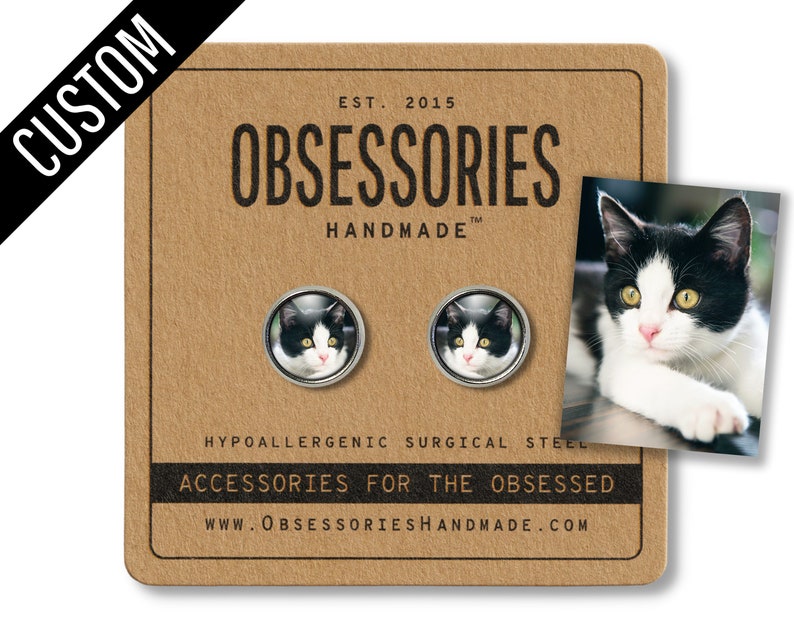 May include: A pair of hypoallergenic surgical steel earrings featuring a black and white cat photo. The earrings are handmade and come with a card that says "OBSESSORIES Handmade" and "Accessories for the obsessed".