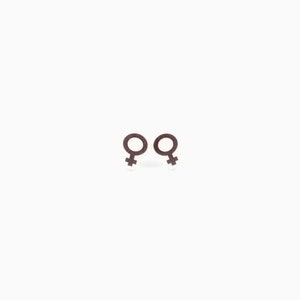 May include: Two brown glittery earrings in the shape of the female gender symbol, set against a white background. The earrings are small and detailed, with a textured appearance. The design is simple and elegant.