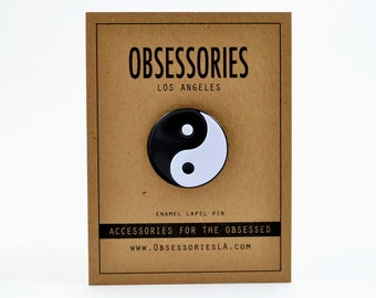 May include: Black and white enamel yin yang lapel pin on a brown card with the text "OBSESSORIES LOS ANGELES ENAMEL LAPEL PIN ACCESSORIES FOR THE OBSESSED WWW.OBSESSORIESLA.COM"