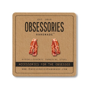 May include: A pair of bacon-shaped earrings on a brown card. The card has the text "OBSESSORIES HANDMADE" and "ACCESSORIES FOR THE OBSESSED". The earrings are red and white, and the card reads "EST. 2015".