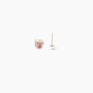 May include: A pair of novelty stud earrings. One earring is a miniature white takeout container with red text that reads "Enjoy". The other earring has a silver post and a white, flower-shaped backing.