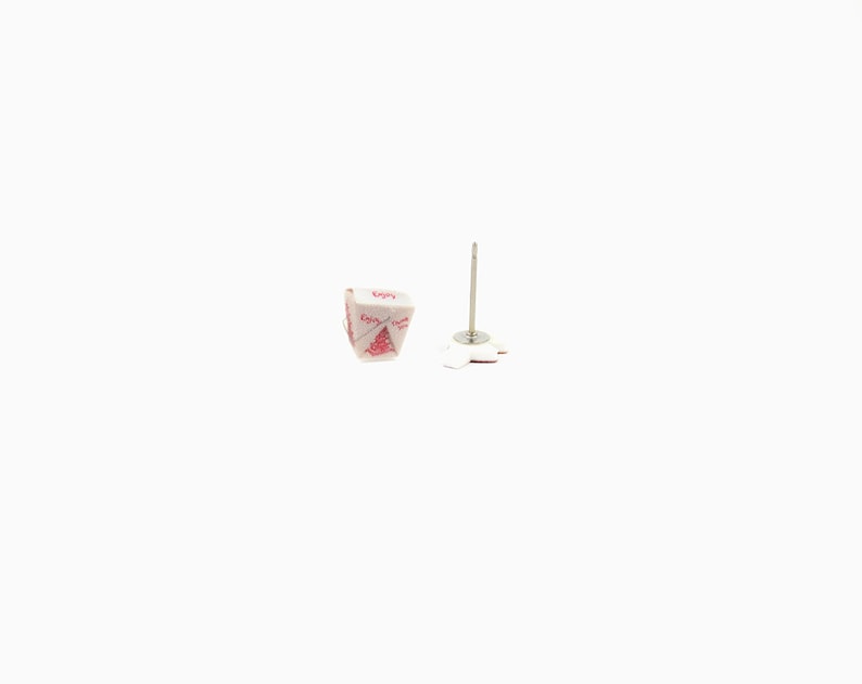 May include: A pair of novelty stud earrings. One earring is a miniature white takeout container with red text that reads "Enjoy". The other earring has a silver post and a white, flower-shaped backing.