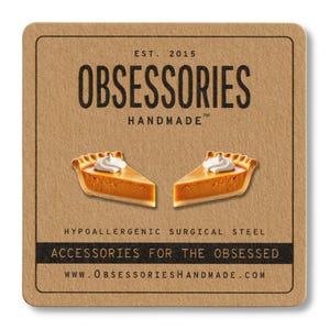 May include: A square, brown card features the text "OBSESSORIES HANDMADE" and two pumpkin pie slice earrings. The earrings have orange filling and white whipped cream. The card also states "ACCESSORIES FOR THE OBSESSED" and "HYPOALLERGENIC SURGICAL STEEL."