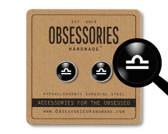 Könnte beinhalten: Ein Paar schwarze und silberne Ohrstecker mit einem weißen Sternzeichen Waage. Die Ohrringe befinden sich auf einem braunen Hintergrund mit dem Text "OBSESSORIES HANDMADE" und "ACCESSORIES FOR THE OBSESSED".