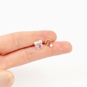 May include: Miniature Chinese takeout box with a red and white design, next to a fortune cookie with a white paper fortune. The box has the word "Enjoy" printed on it. The items are small and appear to be dollhouse accessories.