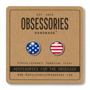 Pode incluir: Um par de pequenos brincos redondos prateados com um design de bandeira americana azul e branca em um brinco e um design de listras vermelhas e brancas no outro brinco. Os brincos est&atilde;o em um cart&atilde;o marrom com o texto "OBSESSORIES HANDMADE" e "ACCESSORIES FOR THE OBSESSED".