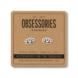 Puede incluir: Pendientes de bot&oacute;n con forma de nudilleras de color plateado sobre una tarjeta marr&oacute;n. La tarjeta tiene el texto "OBSESSORIES HANDMADE" y "ACCESSORIES FOR THE OBSESSED". Los pendientes son de acero quir&uacute;rgico hipoalerg&eacute;nico.