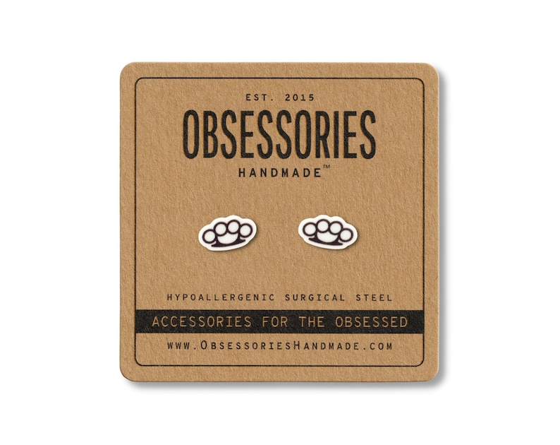 Puede incluir: Pendientes de bot&oacute;n con forma de nudilleras de color plateado sobre una tarjeta marr&oacute;n. La tarjeta tiene el texto "OBSESSORIES HANDMADE" y "ACCESSORIES FOR THE OBSESSED". Los pendientes son de acero quir&uacute;rgico hipoalerg&eacute;nico.