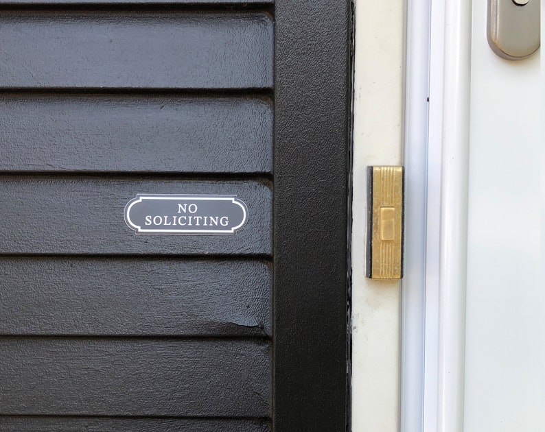 Puede incluir: Una puerta negra con un letrero blanco que dice "No Soliciting" y un bot&oacute;n de timbre dorado.