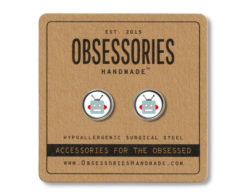 May include: A pair of silver robot earrings with red accents. The earrings are on a brown card with the text "OBSESSORIES HANDMADE" and "ACCESSORIES FOR THE OBSESSED".