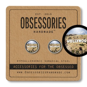 May include: A pair of silver-toned pinback buttons with a photo of the Hollywood sign. The buttons are on a brown background with the text "OBSESSORIES HANDMADE" and "ACCESSORIES FOR THE OBSESSED".