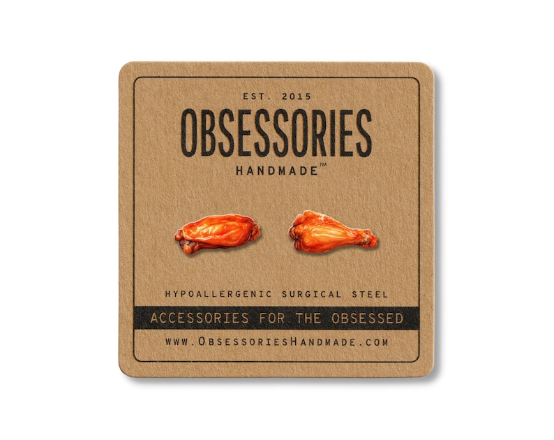 Puede incluir: Una tarjeta cuadrada marr&oacute;n con el texto "OBSESSORIES HANDMADE" y dos ilustraciones de alitas de pollo. La tarjeta tambi&eacute;n incluye el texto "ACCESSORIES FOR THE OBSESSED" y "WWW.OBSESSORIESHANDMADE.COM".