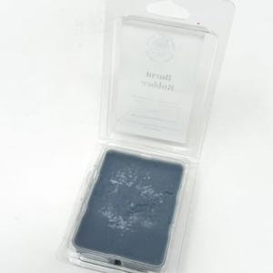 May include: A rectangular, dark blue ink pad with white residue, encased in a clear plastic clamshell package. The package has a hanging hole at the top. The ink pad is likely for stamping or printing.