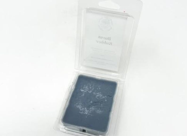 May include: A rectangular, dark blue ink pad with white residue, encased in a clear plastic clamshell package. The package has a hanging hole at the top. The ink pad is likely for stamping or printing.