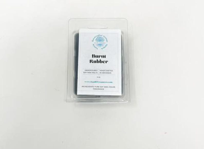 May include: A package of soy wax melts in a clear plastic container. The label reads "Burnt Rubber" with additional text. The wax is dark gray. The product is hand-poured and made with pure soy wax.