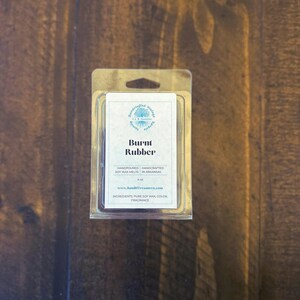 May include: A clear plastic package containing soy wax melts. The label reads "Burnt Rubber" and lists ingredients. The product is hand-poured in Arkansas and weighs 4 oz.
