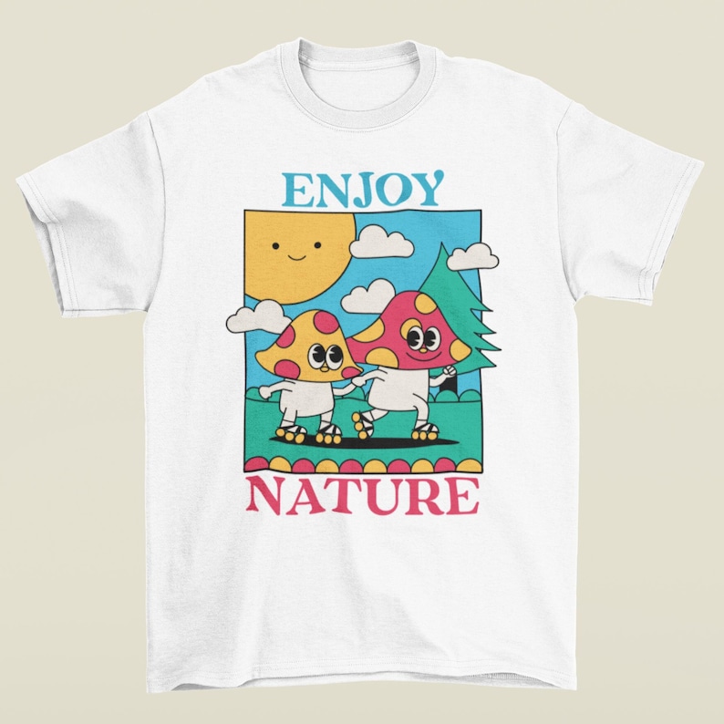 A white Enjoy Nature t-shirt lays flat, featuring a playful design of mushrooms holding hands and rollerblading under the sun. The cheerful, nature-inspired graphic evokes a sense of fun and positivity, perfect for mushroom lovers.