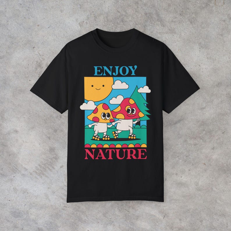 A black Enjoy Nature t-shirt lays flat, featuring a playful design of mushrooms holding hands and rollerblading under the sun. The cheerful, nature-inspired graphic evokes a sense of fun and positivity, perfect for mushroom lovers.