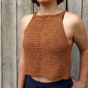 Puede incluir: Un top de crochet marrón con tirantes y escote cuadrado. El top es corto y tiene un corte holgado.