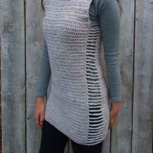 May include: A gray crocheted sleeveless turtleneck top with a long, asymmetrical hemline. The top has a slit on the side and a ribbed texture.