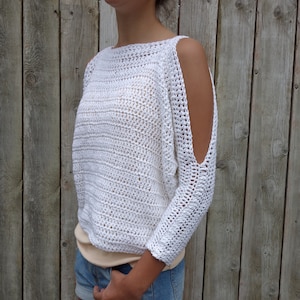 Puede incluir: Top blanco de crochet con detalle de hombros descubiertos. El top tiene un corte holgado y está hecho con un hilo ligero.