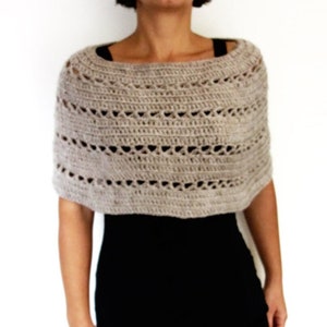 May include: A beige crochet shawl with a delicate openwork pattern. The shawl is worn over a black dress.