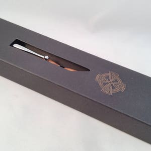 May include: A silver pen with a wooden barrel in a gray box with a Celtic knot design.