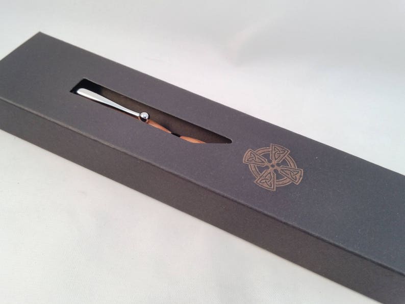 May include: A silver pen with a wooden barrel in a gray box with a Celtic knot design.