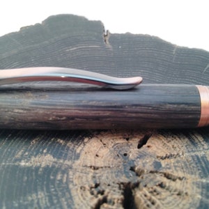 May include: A wooden pen with a copper band and a silver clip. The pen is resting on a wooden surface.