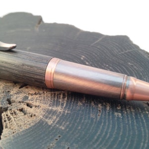 May include: A wooden pen with a copper and silver finish. The pen has a dark wood body and a copper tip.
