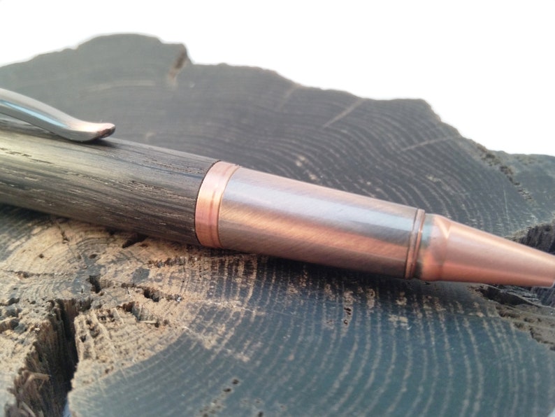 May include: A wooden pen with a copper and silver finish. The pen has a dark wood body and a copper tip.
