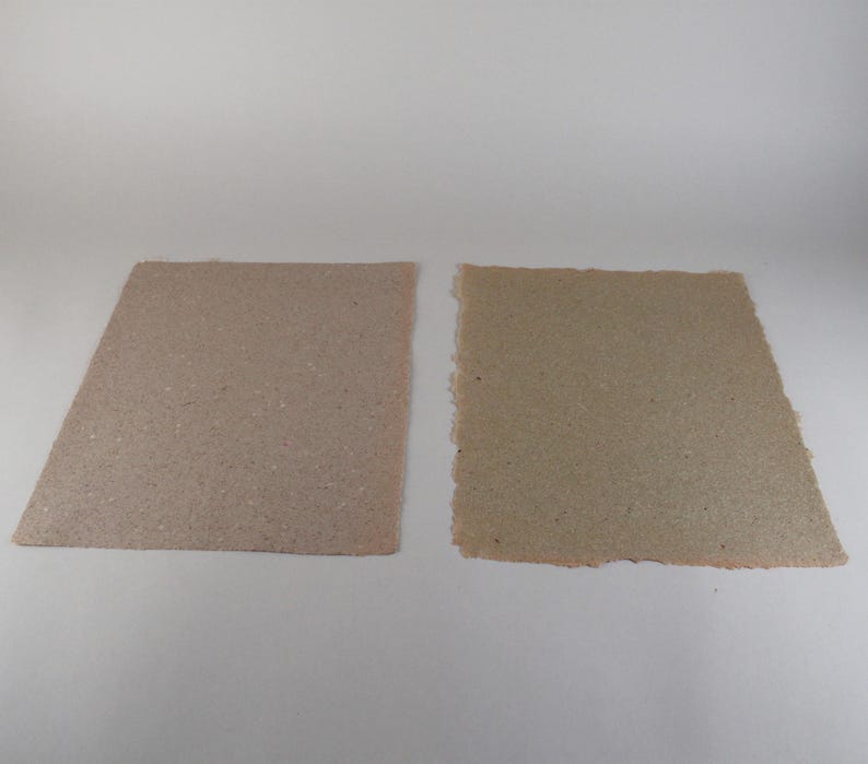 May include: Two handmade paper sheets in shades of brown and tan. The sheet on the left has a clean, angled edge, while the sheet on the right has a rough, torn edge. Both have a speckled texture.