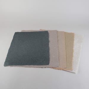 May include: A stack of handmade paper sheets in various neutral colors. The sheets include shades of gray, beige, and white, with a textured surface and deckled edges. The paper is arranged on a white background.