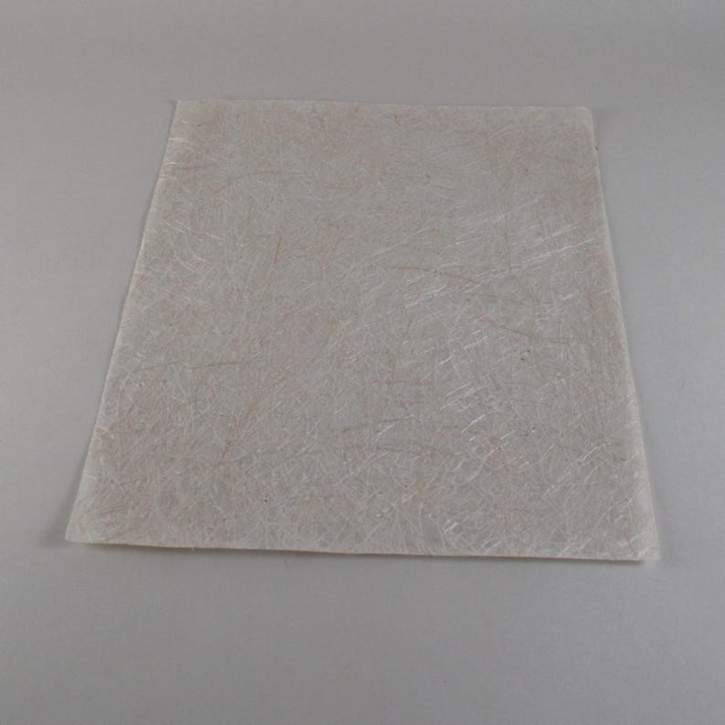 May include: A rectangular, off-white sheet with a fibrous texture. The material appears to be a composite, with visible strands creating a subtle, irregular pattern across the surface. The sheet is set against a neutral background.