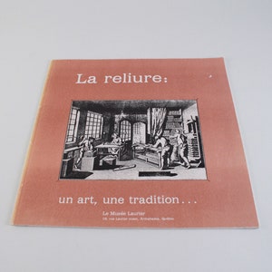 May include: A brochure with a salmon-colored cover featuring the text "La reliure: un art, une tradition..." in white. The brochure includes a black and white illustration of people working in a workshop. The text "Le Musée Laurier" is also visible.