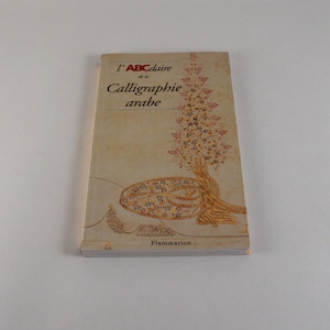 Peut inclure: Un livre à couverture rigide intitulé "L'ABCdaire de la Calligraphie arabe" avec une couverture beige. La couverture présente une illustration d'arbre et un motif orné. Le livre est publié par Flammarion.