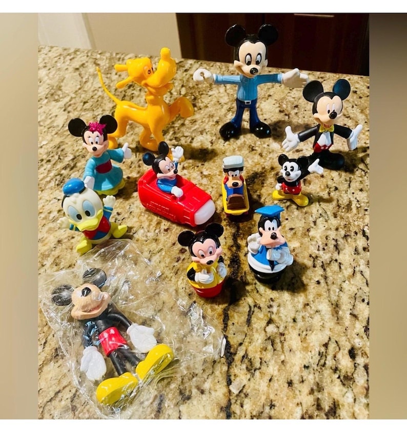 May include: A collection of colorful Mickey Mouse and friends figurines. The figurines include Mickey Mouse, Minnie Mouse, Donald Duck, Pluto, and others. The figures are in various poses and outfits, with bright colors.