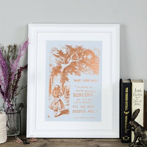 May include: A framed print featuring a copper foil design of a scene from Alice in Wonderland. The quote "HAVE I GONE MAD?" is featured with the text "I'm afraid so, you're entirely BONKERS. But I'll tell you a secret..... ALL THE BEST PEOPLE ARE."