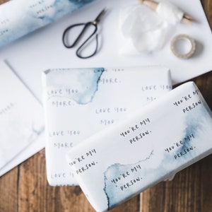Puede incluir: Dos cajas de regalo envueltas en papel blanco con un dise&ntilde;o de acuarela azul. Las cajas tienen el texto "You're my person." repetido.