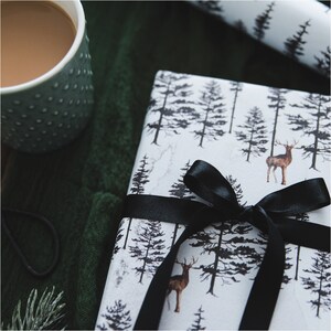 May include: A white gift wrap with a black ribbon and a forest scene with deer and trees.