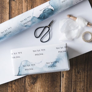 Puede incluir: Papel de regalo blanco con dise&ntilde;os azules de acuarela y el texto repetido "You're My Person." Se muestra un rollo de papel de regalo con una caja de regalo envuelta en el mismo papel.
