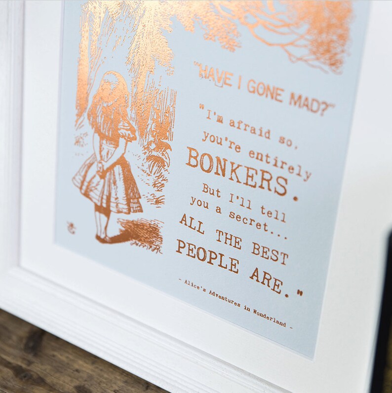 May include: A framed print with a copper foil design featuring Alice from Alice in Wonderland. The quote reads "Have I gone mad?" "I'm afraid so, you're entirely bonkers. But I'll tell you a secret... All the best people are." - Alice's Adventures in Wonderland