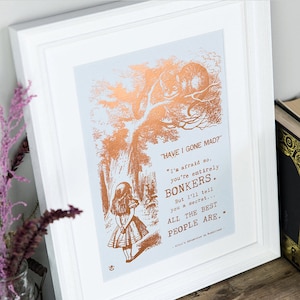 May include: A framed print with a copper foil design featuring a quote from Alice in Wonderland. The quote reads "HAVE I GONE MAD?" "I'm afraid so. You're entirely BONKERS. But I'll tell you a secret... ALL THE BEST PEOPLE ARE..."