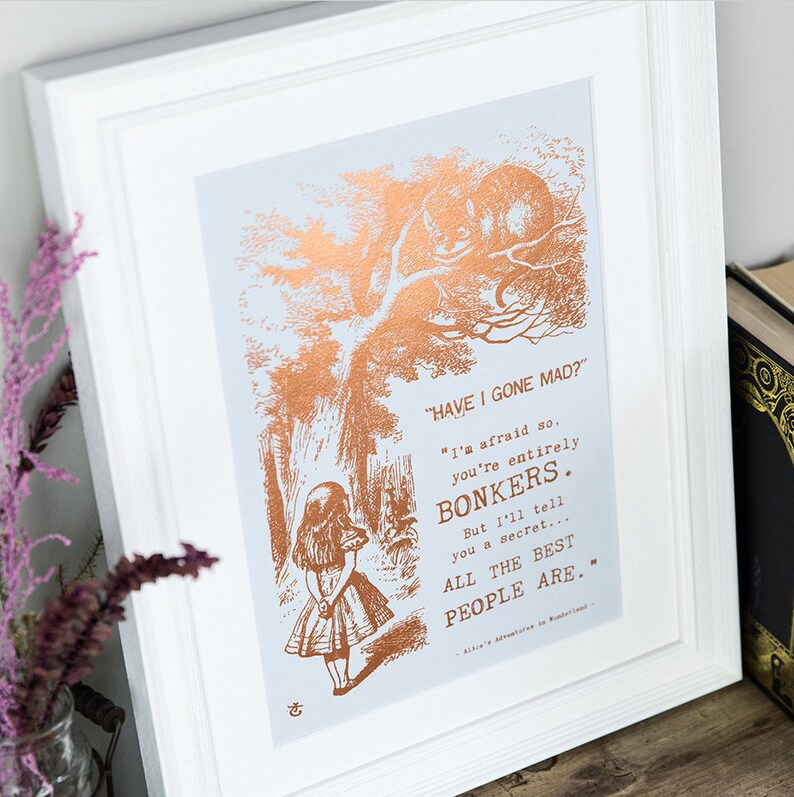 May include: A framed print with a copper foil design featuring a quote from Alice in Wonderland. The quote reads "HAVE I GONE MAD?" "I'm afraid so. You're entirely BONKERS. But I'll tell you a secret... ALL THE BEST PEOPLE ARE..."