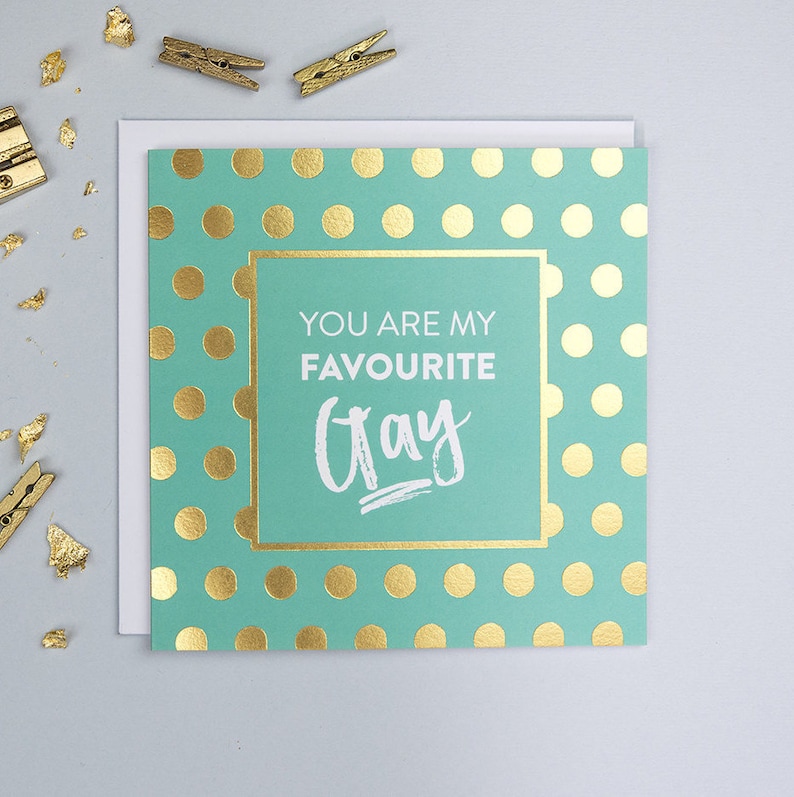 Pu&ograve; includere: Un biglietto verde chiaro con pois dorati e una cornice dorata. Il testo all'interno della cornice dice "You are my favourite Gray".