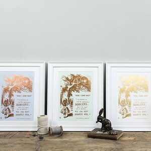 May include: Three white framed prints with gold foil accents. Each print features a black and white illustration of Alice in Wonderland with a quote from the book. The quote reads "Have I gone mad? I'm afraid so. You're entirely bonkers. But I'll tell you a secret. All the best people are."