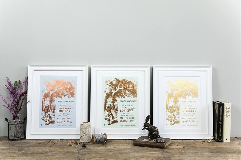 May include: Three white framed prints with gold foil accents. Each print features a black and white illustration of Alice in Wonderland with a quote from the book. The quote reads "Have I gone mad? I'm afraid so. You're entirely bonkers. But I'll tell you a secret. All the best people are."