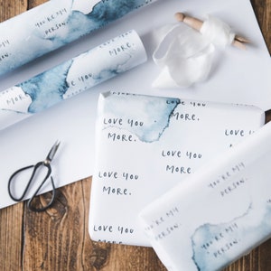 May include: White gift wrap with blue watercolour designs and the text "Love you more" and "You're my person" repeated.